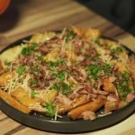 Delicious loaded potato wedges garnished with bacon, cheese, and fresh parsley served on a wooden table.