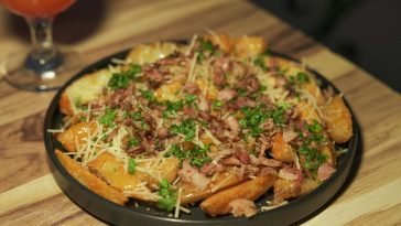Delicious loaded potato wedges garnished with bacon, cheese, and fresh parsley served on a wooden table.