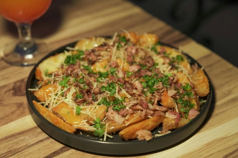 Delicious loaded potato wedges garnished with bacon, cheese, and fresh parsley served on a wooden table.