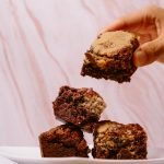A stack of delicious homemade brownies being picked up by hand, perfect for dessert lovers.