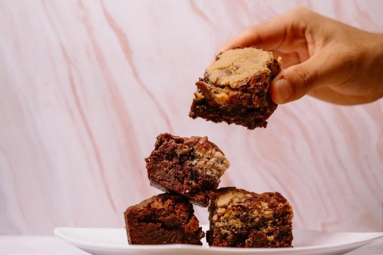 A stack of delicious homemade brownies being picked up by hand, perfect for dessert lovers.