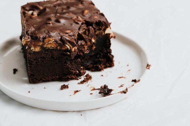Decadent chocolate brownie with nuts on a white plate, perfect for dessert lovers.
