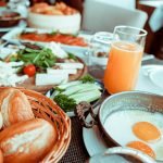 Appetizing breakfast table with orange juice, fried eggs, breads, and fresh vegetables.