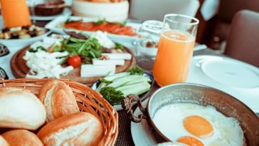 Appetizing breakfast table with orange juice, fried eggs, breads, and fresh vegetables.