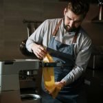 Chef expertly makes fresh pasta in a professional kitchen using a pasta machine.