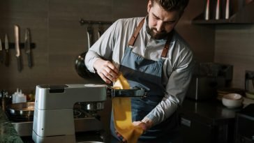 Chef expertly makes fresh pasta in a professional kitchen using a pasta machine.