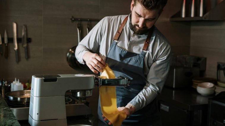 Chef expertly makes fresh pasta in a professional kitchen using a pasta machine.