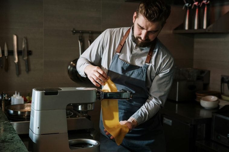 Chef expertly makes fresh pasta in a professional kitchen using a pasta machine.