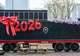 A festive train decorated with '2026' and a red bow, set in an urban environment.
