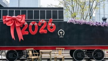 A festive train decorated with '2026' and a red bow, set in an urban environment.