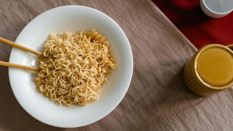 A delicious serving of instant noodles in a white bowl with chopsticks on a textured table.
