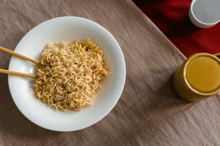 A delicious serving of instant noodles in a white bowl with chopsticks on a textured table.