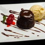 Delicious chocolate lava cake served with vanilla ice cream and cherries on a white plate.