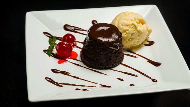 Delicious chocolate lava cake served with vanilla ice cream and cherries on a white plate.