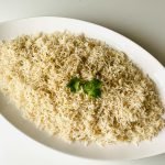 Top view of herb-infused steamed rice garnished with fresh cilantro on a white platter.