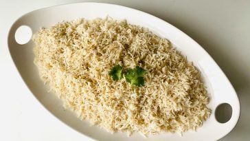 Top view of herb-infused steamed rice garnished with fresh cilantro on a white platter.