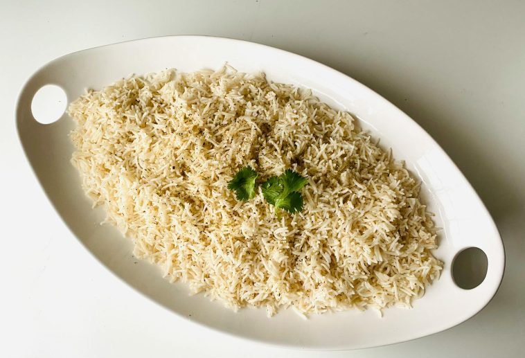 Top view of herb-infused steamed rice garnished with fresh cilantro on a white platter.