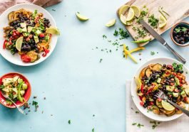 Colorful Mexican salad with avocado, black beans, and lime on a light blue surface.