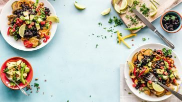 Colorful Mexican salad with avocado, black beans, and lime on a light blue surface.