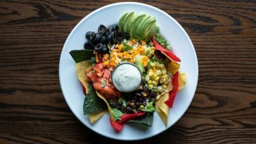 Colorful plate of nachos with fresh avocado, olives, tomatoes, and cheese for a tasty Mexican meal.
