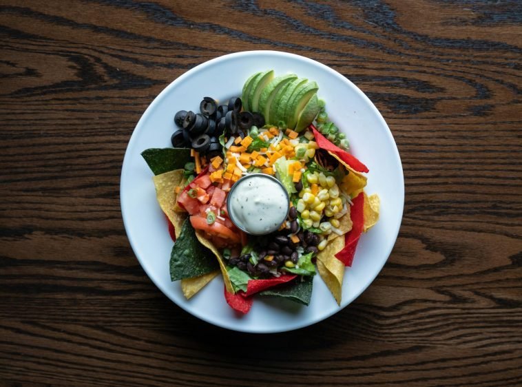 Colorful plate of nachos with fresh avocado, olives, tomatoes, and cheese for a tasty Mexican meal.