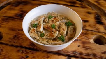 Appetizing chicken pasta dish garnished with herbs in a white bowl on rustic wooden table.