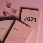 Top view of modern paper calendars with numbers and words near metal clips on pink background