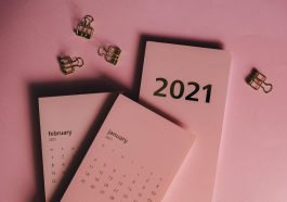 Top view of modern paper calendars with numbers and words near metal clips on pink background