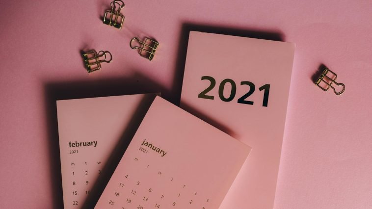Top view of modern paper calendars with numbers and words near metal clips on pink background