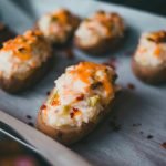 Mouth-watering stuffed baked potatoes with cheese and herbs on parchment paper.