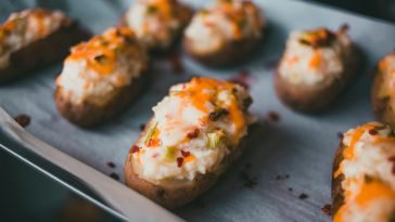Mouth-watering stuffed baked potatoes with cheese and herbs on parchment paper.