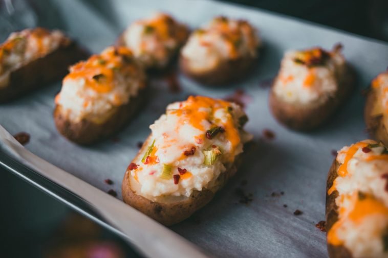 Mouth-watering stuffed baked potatoes with cheese and herbs on parchment paper.