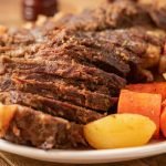 Tender pot roast served with carrots and potatoes on a white plate.