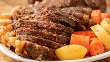Tender pot roast served with carrots and potatoes on a white plate.