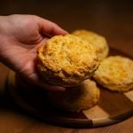 Close-up of a hand reaching for freshly baked biscuits on a wooden board, warm lighting.