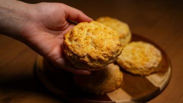 Close-up of a hand reaching for freshly baked biscuits on a wooden board, warm lighting.