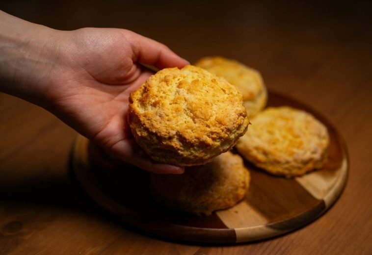 Close-up of a hand reaching for freshly baked biscuits on a wooden board, warm lighting.