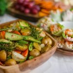 Colorful roasted vegetables with fresh herbs and spring rolls on a wooden platter.