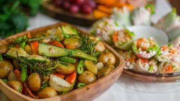 Colorful roasted vegetables with fresh herbs and spring rolls on a wooden platter.