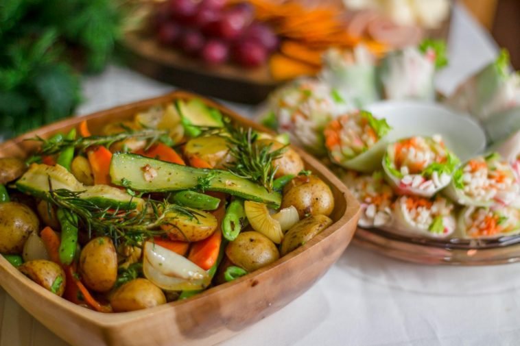 Colorful roasted vegetables with fresh herbs and spring rolls on a wooden platter.