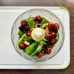 A top-down view of fresh pesto ingredients including basil, hazelnuts, and walnuts in a blender.