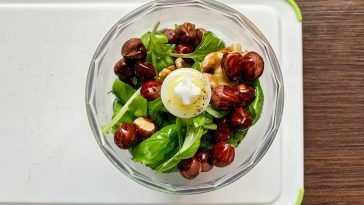 A top-down view of fresh pesto ingredients including basil, hazelnuts, and walnuts in a blender.