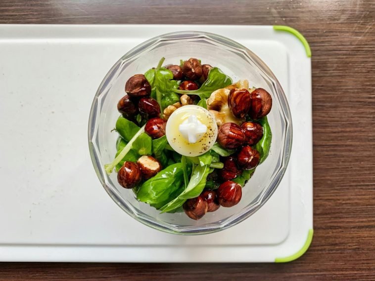 A top-down view of fresh pesto ingredients including basil, hazelnuts, and walnuts in a blender.