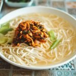 Close-up of a delicious Asian noodle bowl topped with savory shredded chicken and vegetables.