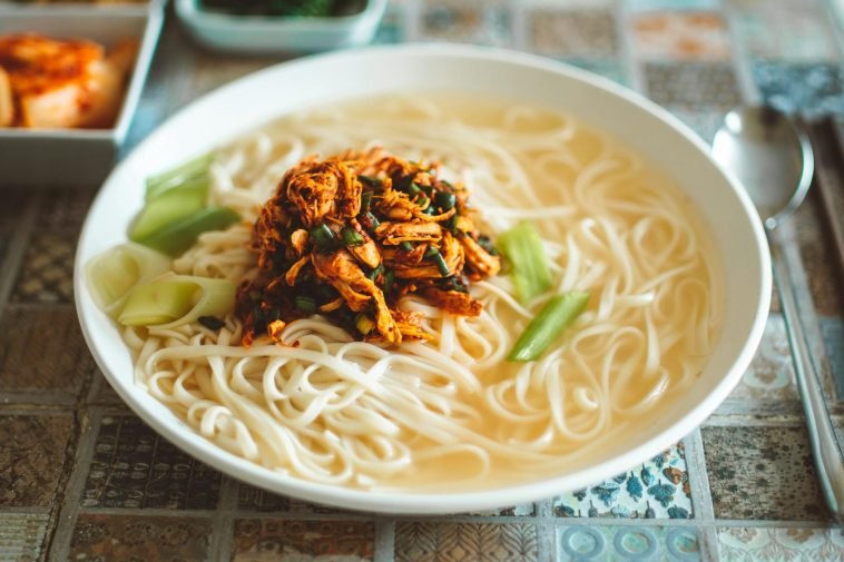 Close-up of a delicious Asian noodle bowl topped with savory shredded chicken and vegetables.