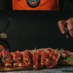 Close-up of a gourmet sandwich being prepared with fresh ingredients and sauces.