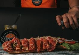 Close-up of a gourmet sandwich being prepared with fresh ingredients and sauces.