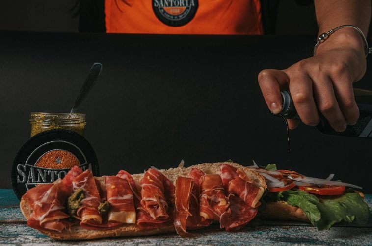 Close-up of a gourmet sandwich being prepared with fresh ingredients and sauces.