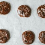 Top view of chocolate cookies with chunks on baking sheet.