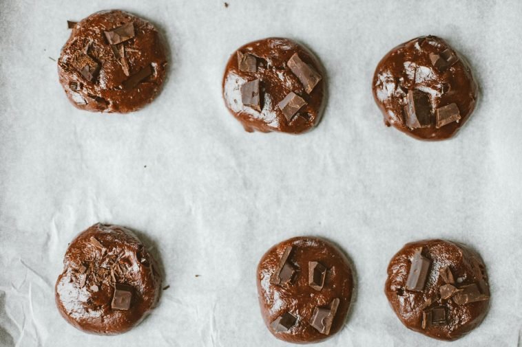 Top view of chocolate cookies with chunks on baking sheet.